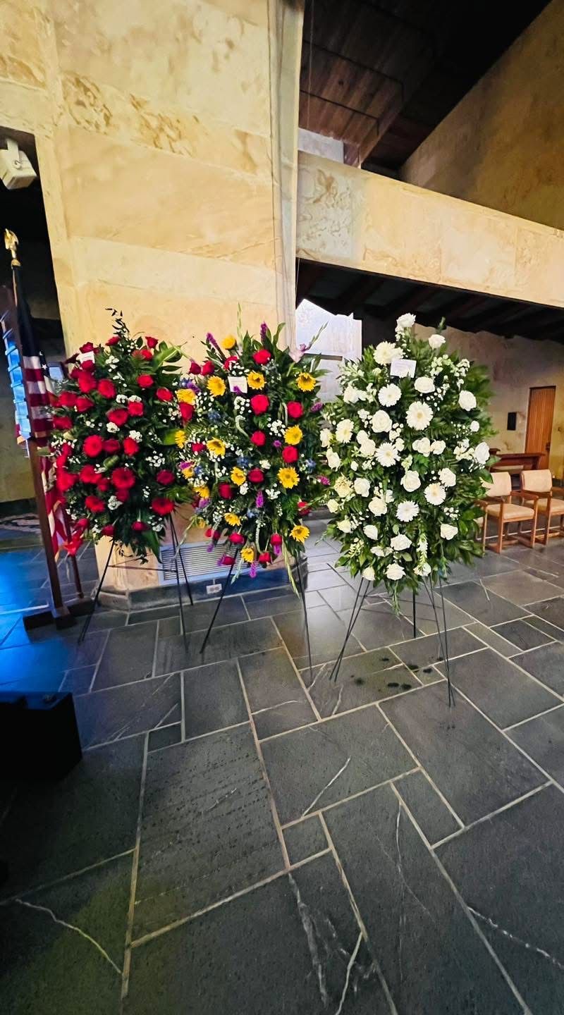 Three floral arrangements on stands in a church. Red and yellow roses, and white flowers.
