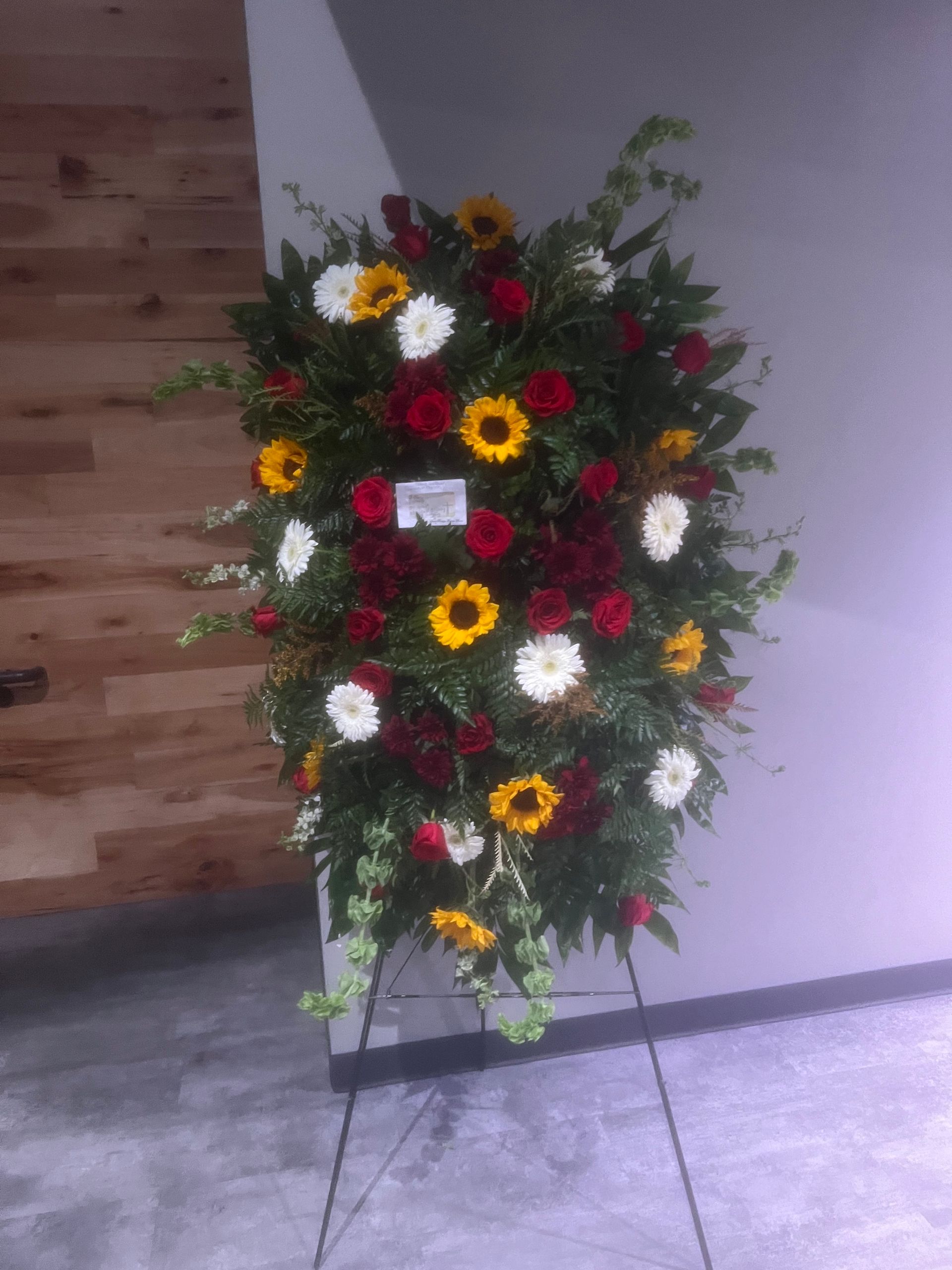 Standing floral arrangement of red, yellow, and white flowers, with greenery.
