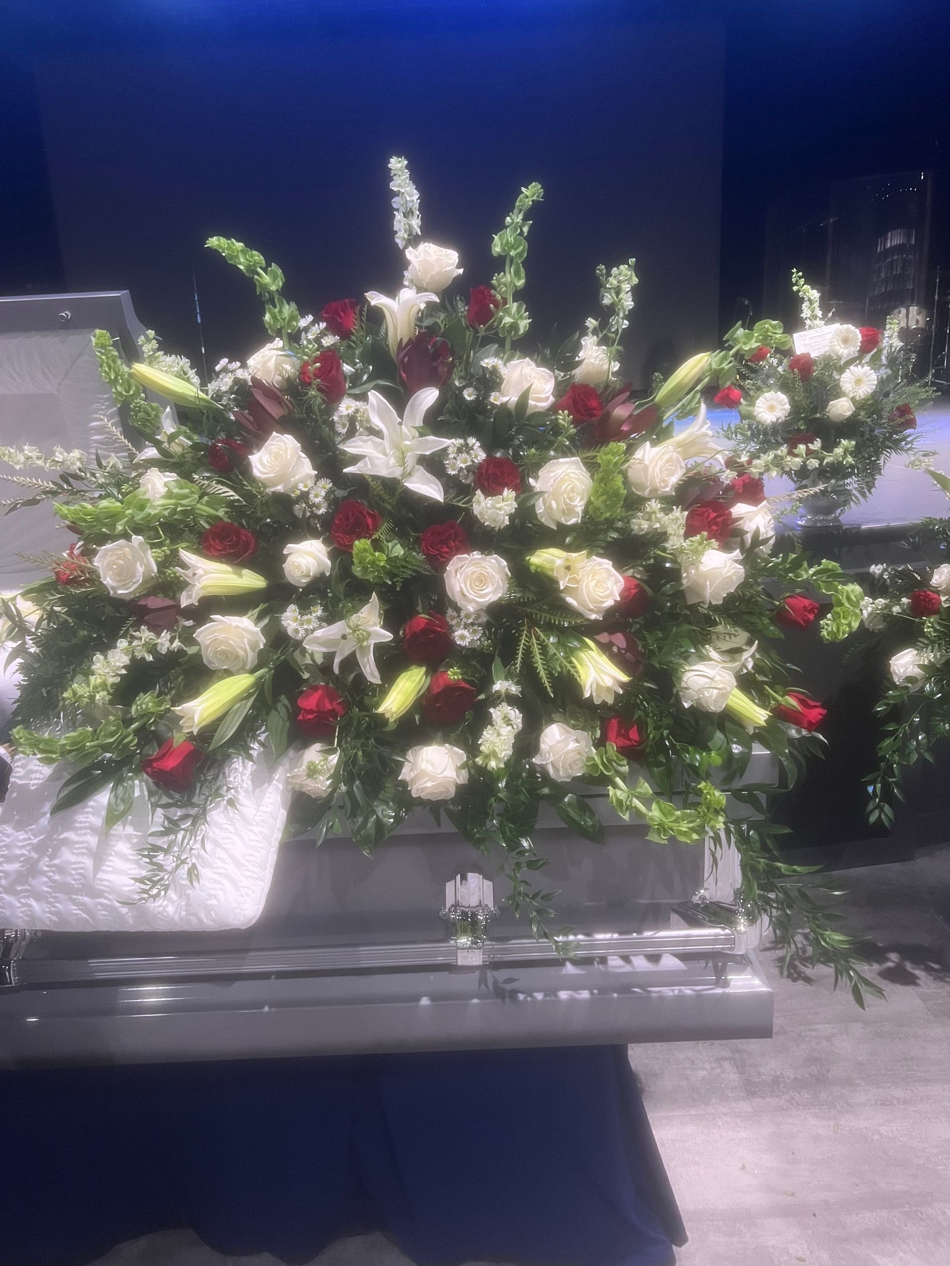 Floral arrangement of white roses, red carnations, and lilies on a casket.
