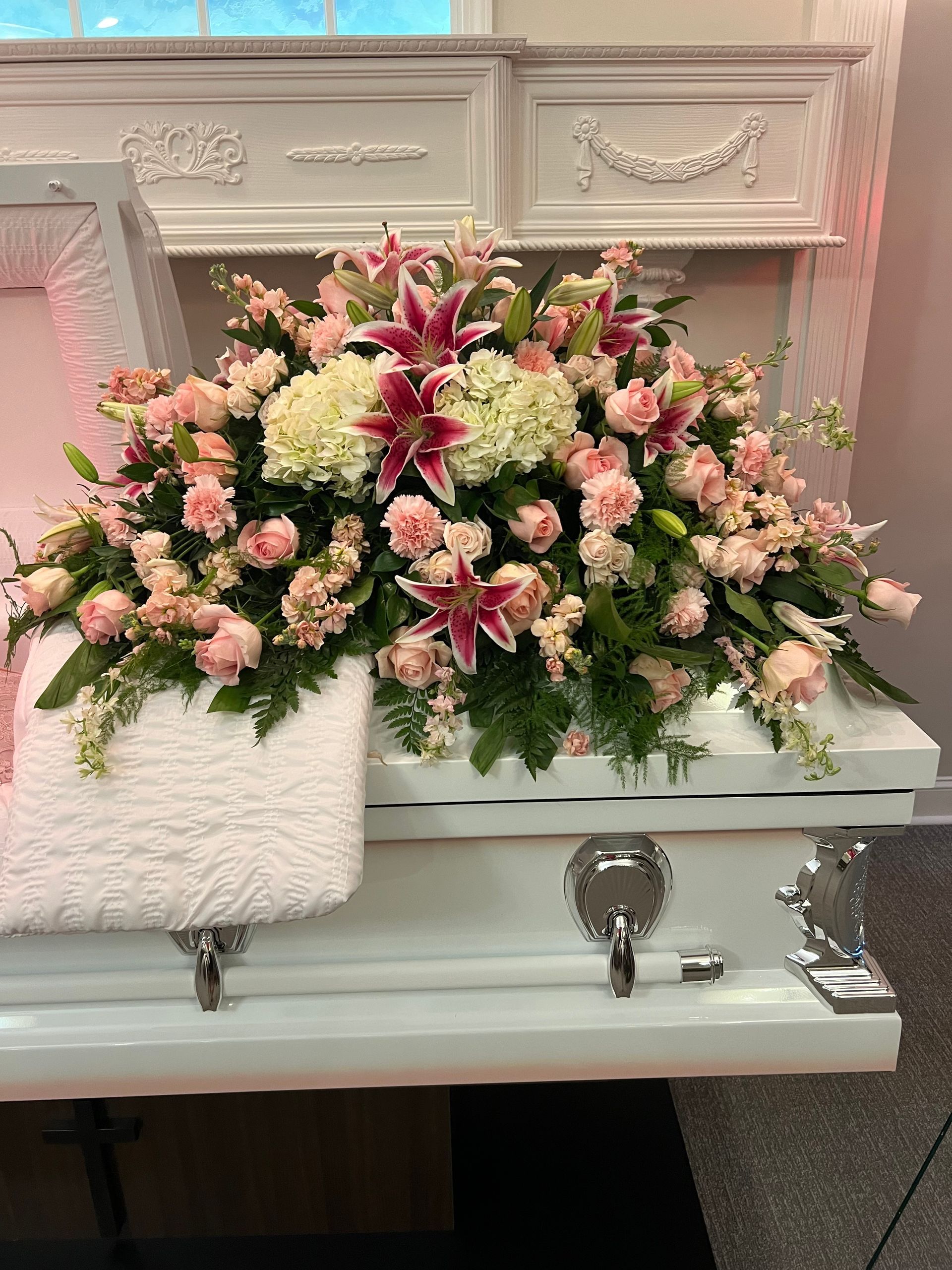 White casket with pink and white floral arrangement.