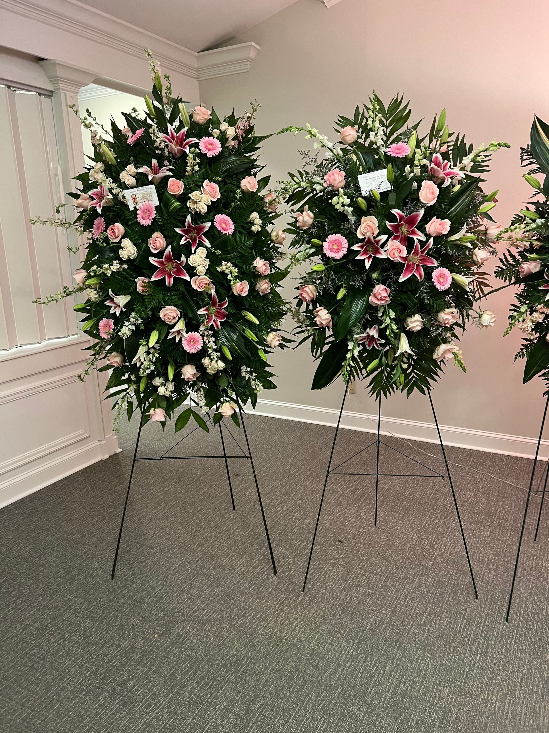 Three floral arrangements on stands in a room. Pink and white flowers with greenery.