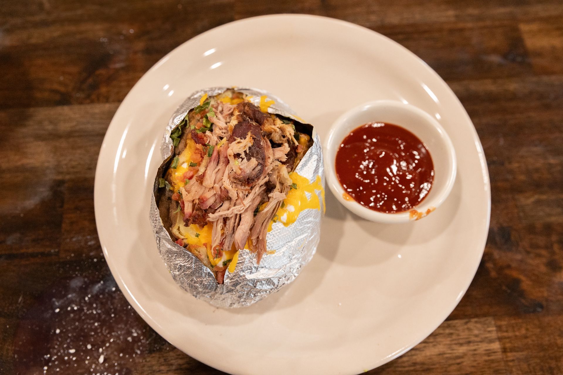 Baked potato loaded with pulled pork and cheese, served with a side of red sauce.