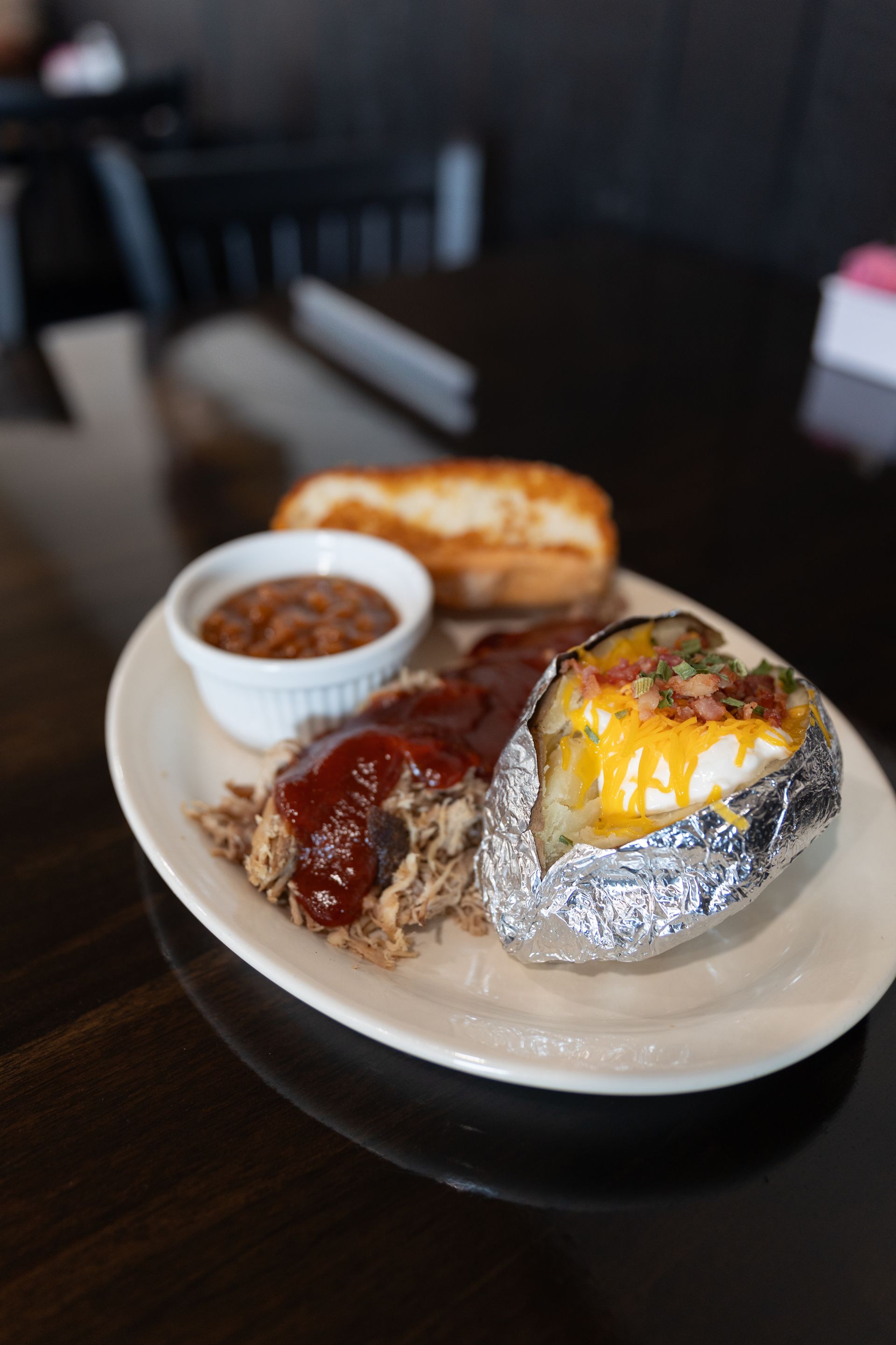 Plate of food: meatloaf with sauce, baked potato, small cup of side, and toasted bread.