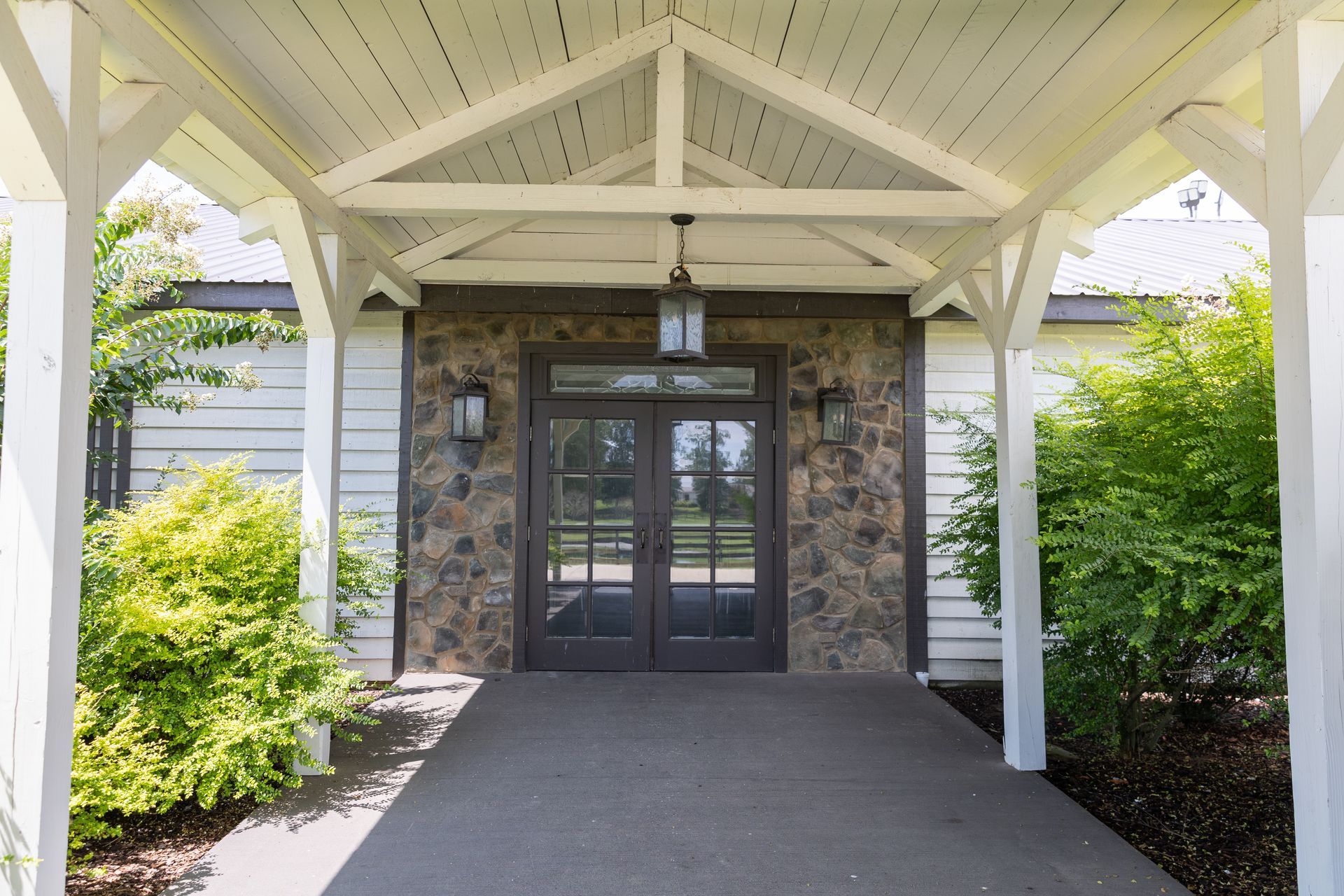 Stone entrance with dark double doors under a white-beamed porch.
