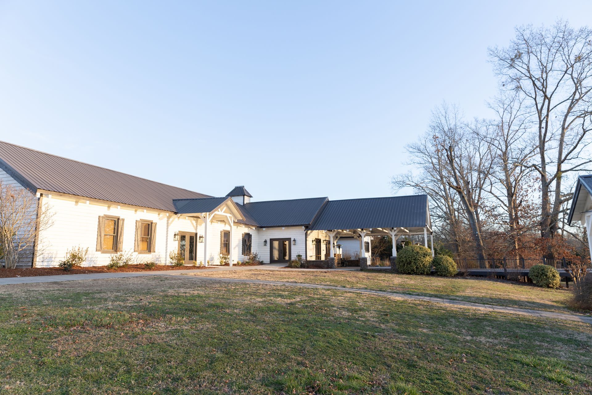 White building with a dark roof and porch on a grassy lawn under a clear sky.