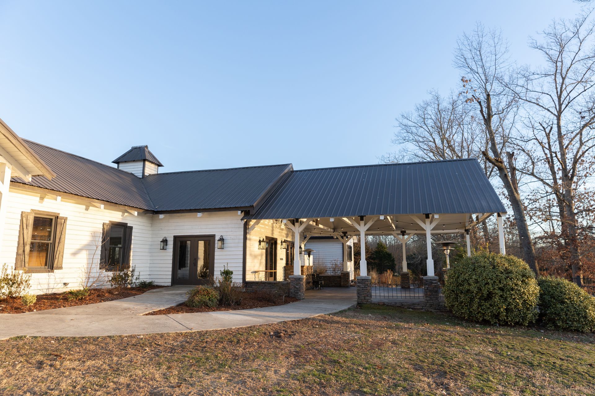 White building with dark roof and covered porch. Outdoors on a sunny day.