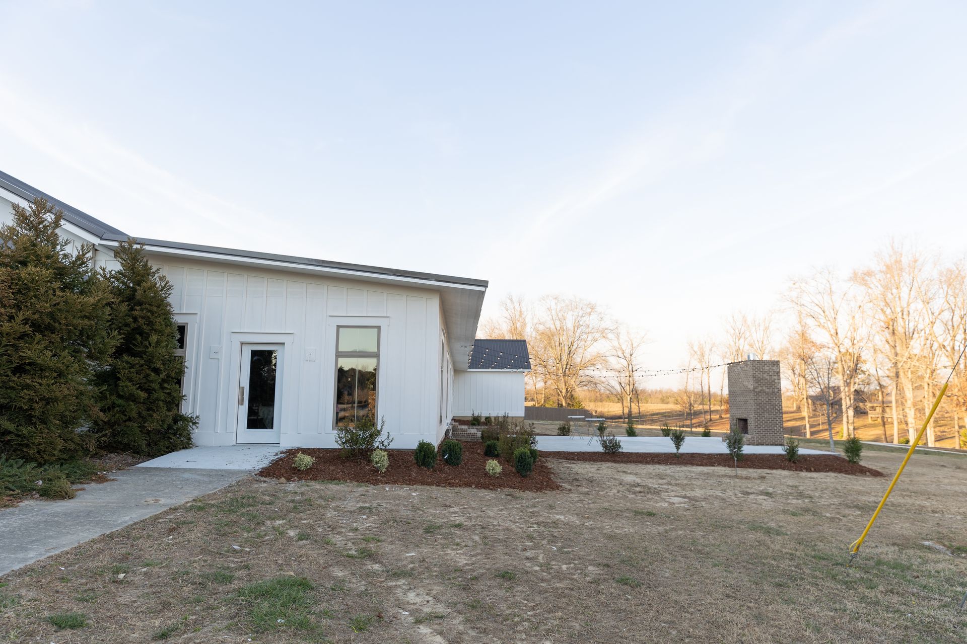 White building with a dark roof and a walkway, trees on the right, and blue sky.