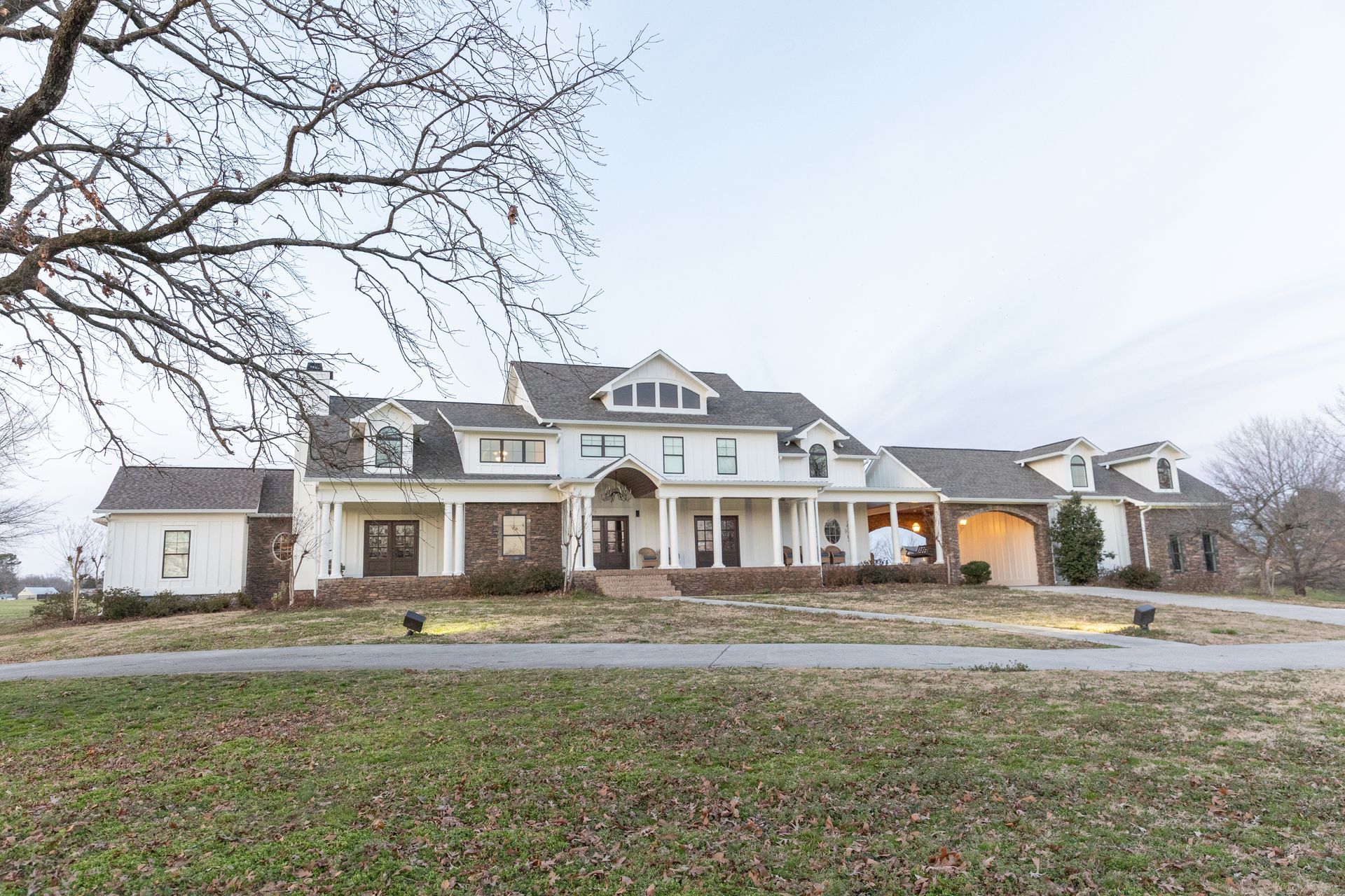 Large white house with columns, a long driveway, and a bare tree.