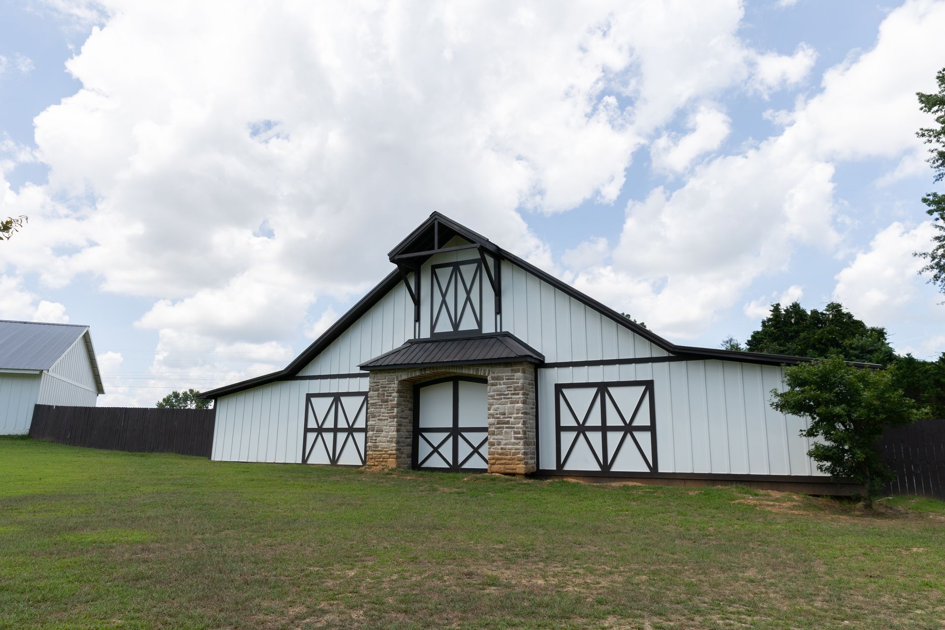 White barn with black trim and stone accents under a cloudy sky.