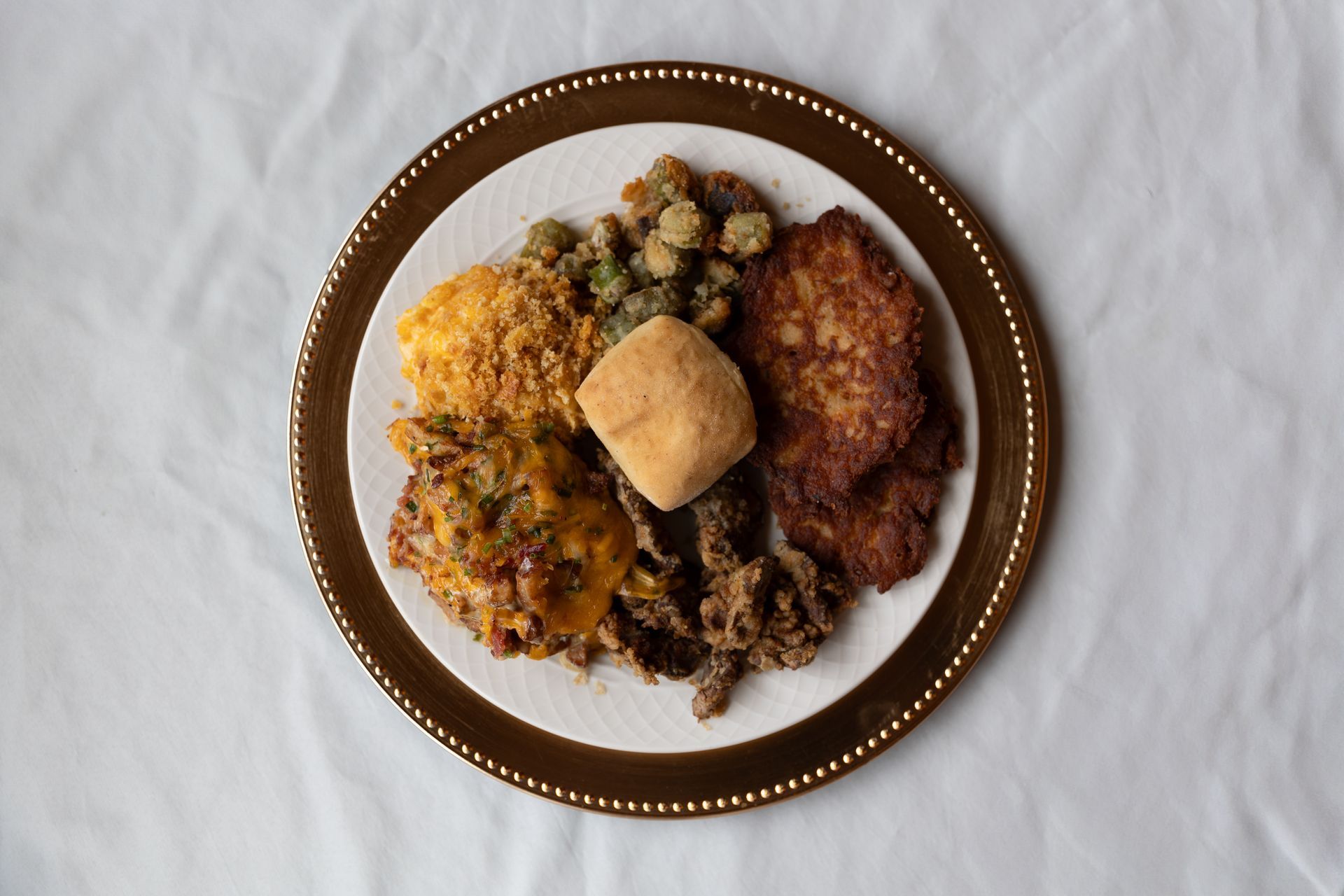 Plate of fried food, including a roll, on a gold-rimmed plate on a white cloth.