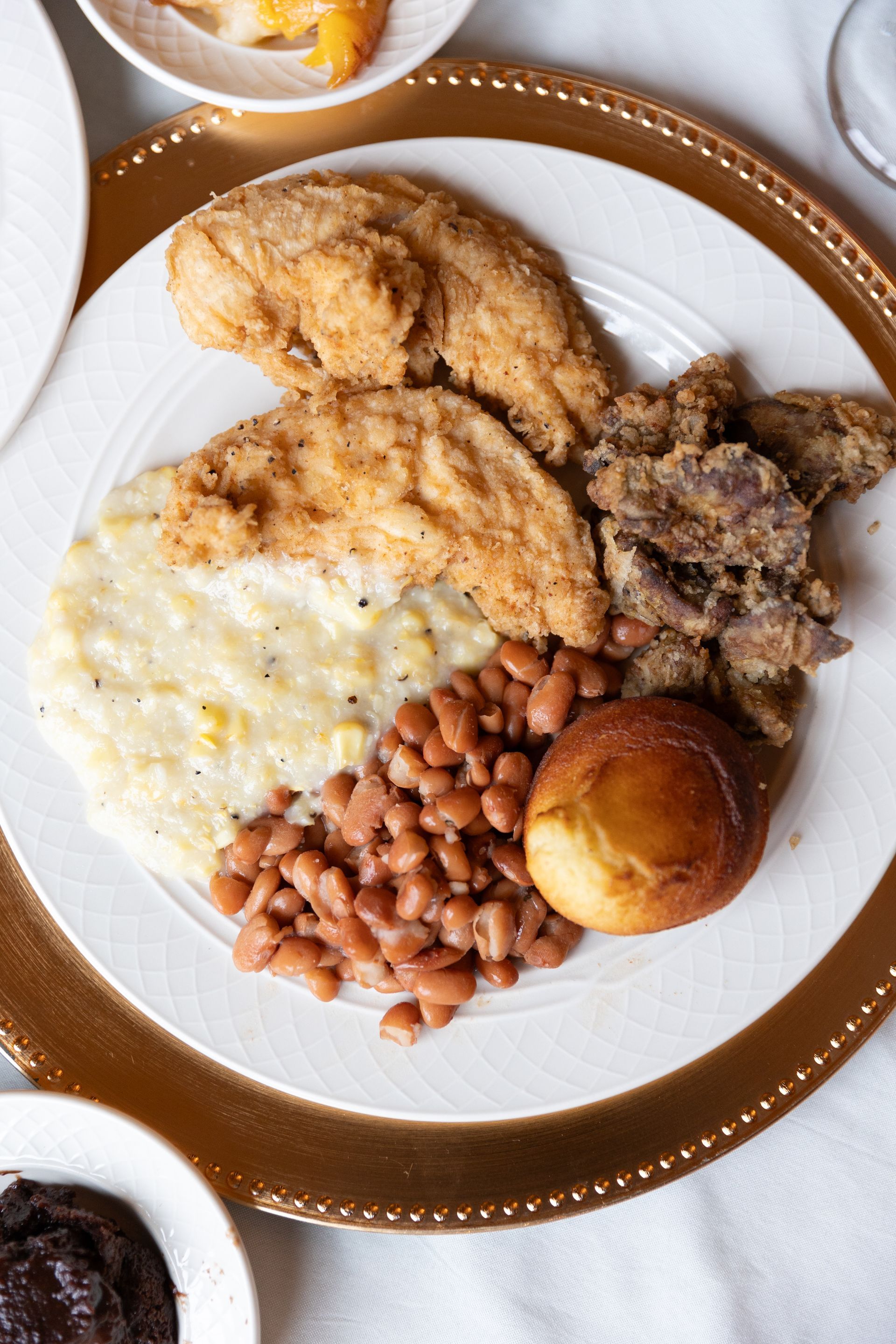 Plate of fried chicken, beans, cornbread, and fried liver on a gold-rimmed plate.