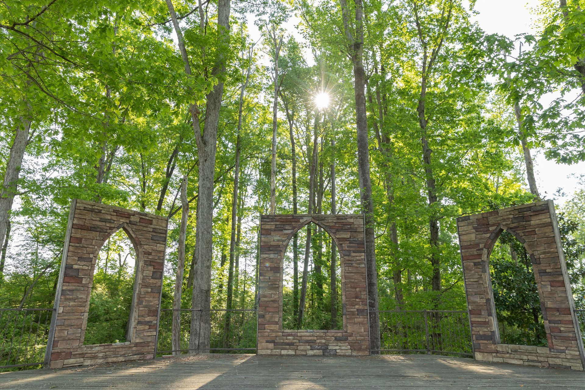 A stone archway in the middle of a forest with the sun shining through the trees.
