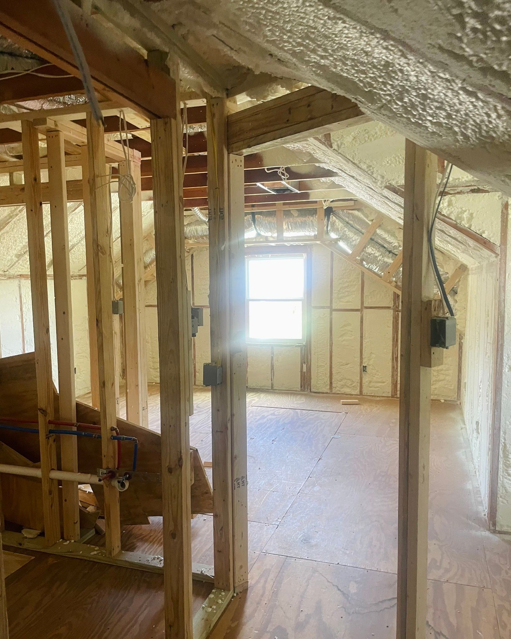 Unfinished attic interior with exposed wood framing, insulation, and a bright window at the far end.
