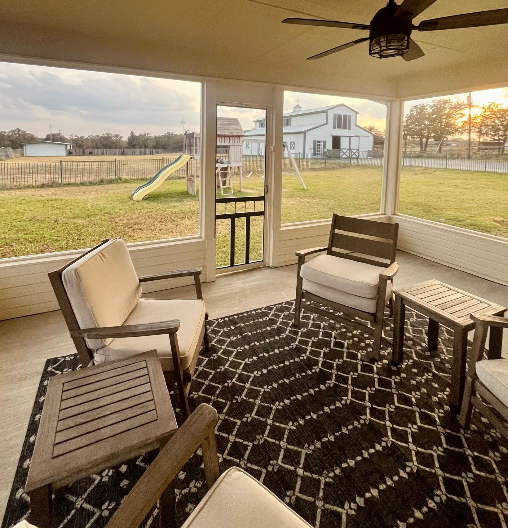 Covered patio with wicker chairs, patterned rug, and a view of a grassy backyard and house at sunset