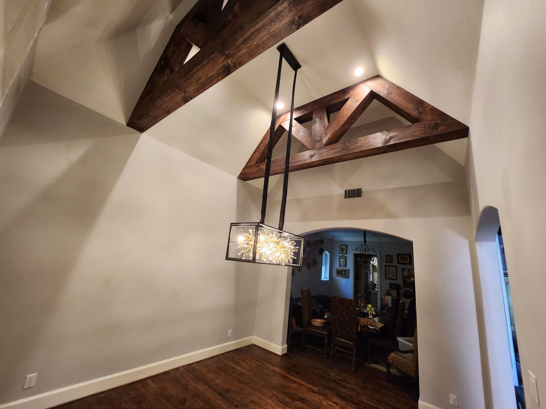 Empty dining room with dark wood beams, hanging lantern light, and an arched doorway.