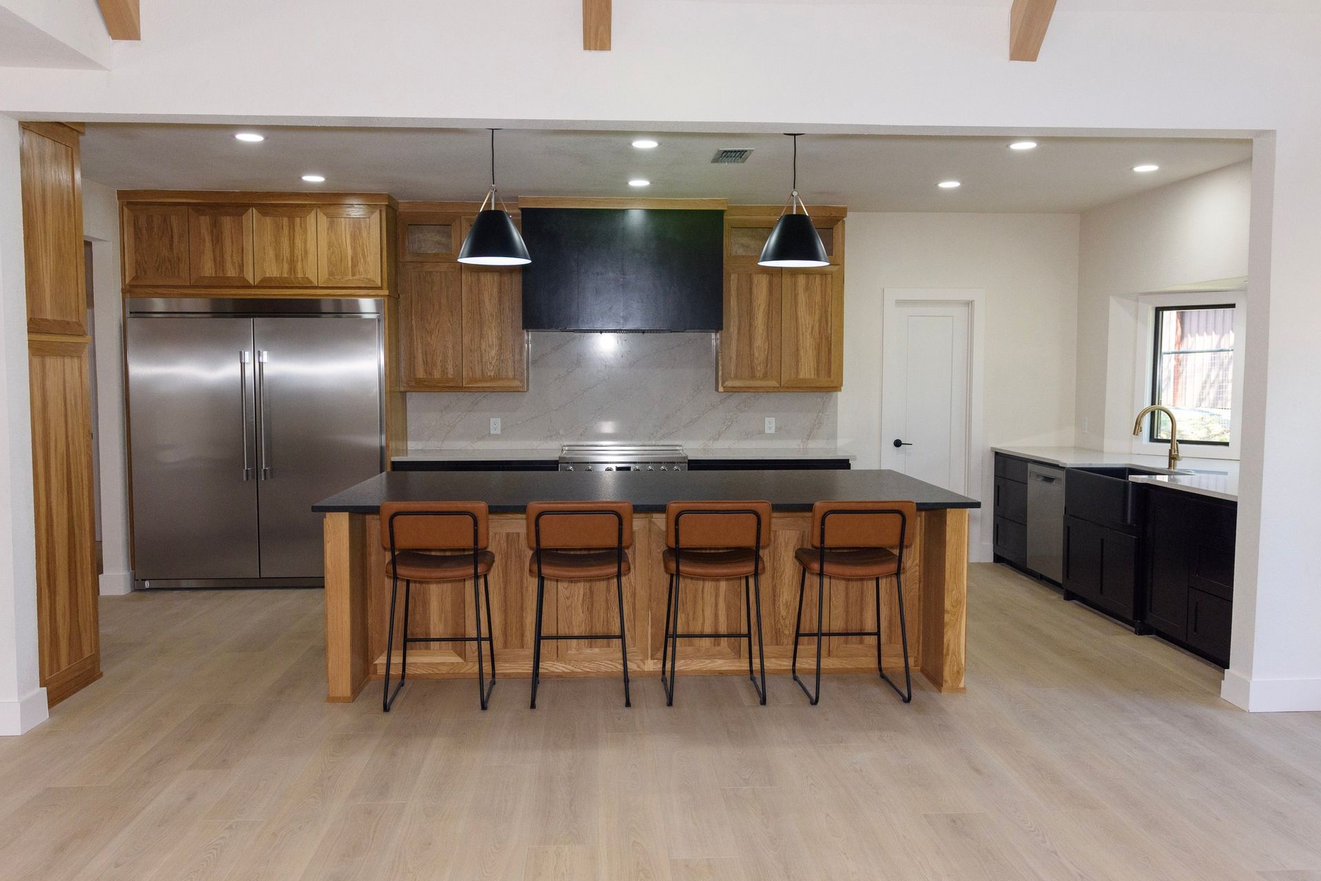 Modern kitchen with stainless steel fridge, island with bar stools, and black cabinets under pendant lights