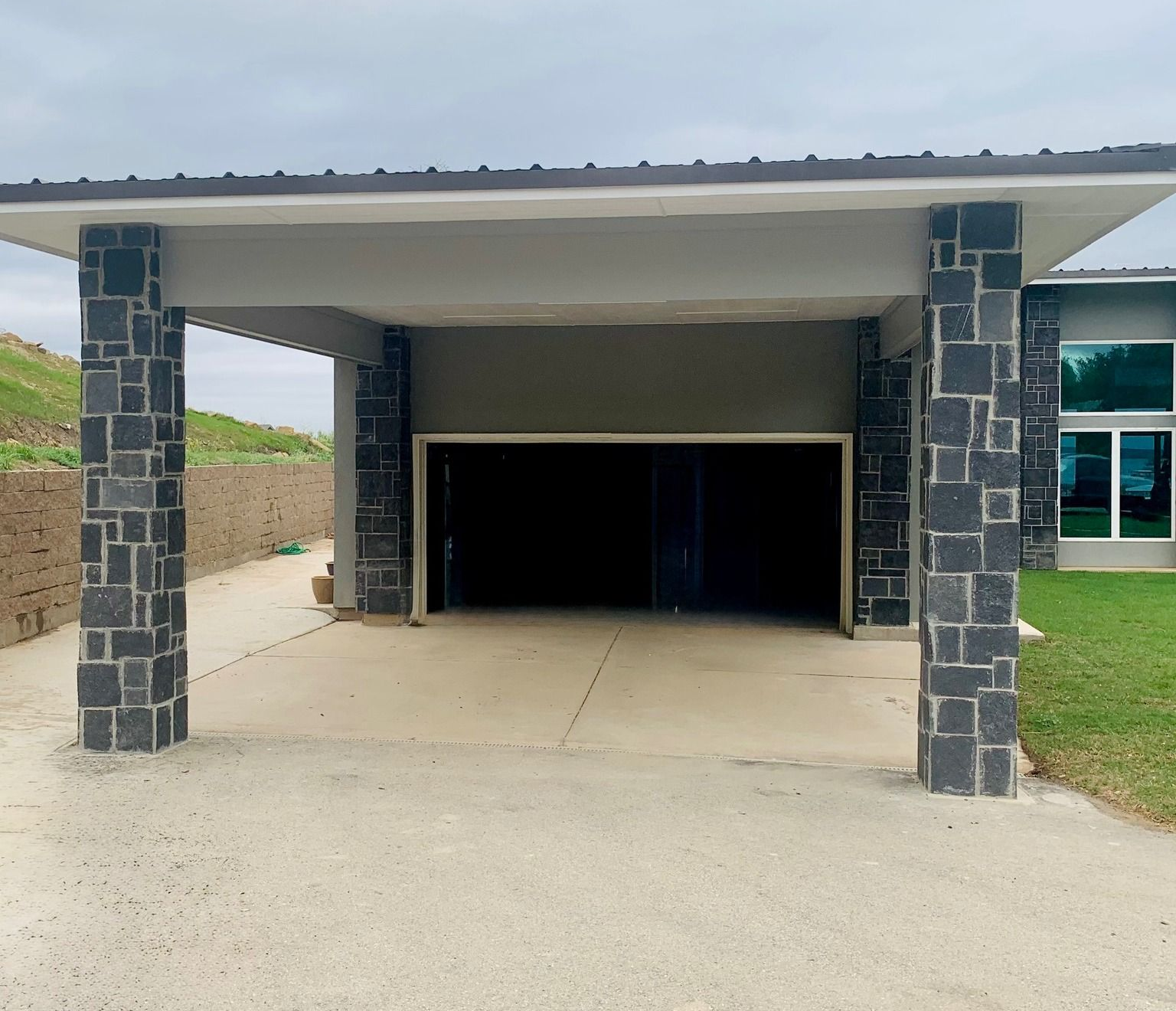 Covered driveway with an open garage, stone pillars, and a concrete entrance.