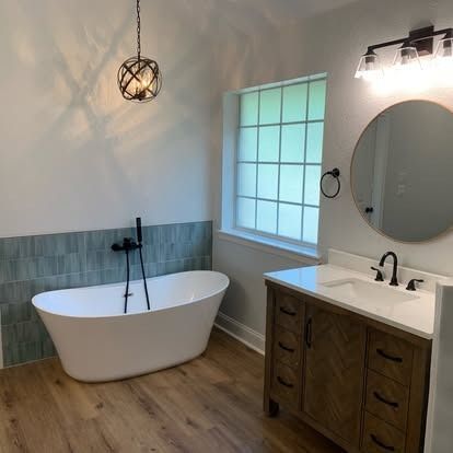 Modern bathroom with freestanding tub, wood vanity, round mirror, and window beside gray tile accent wall