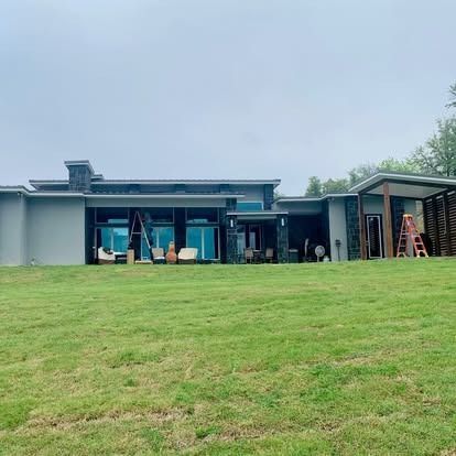 Modern house with large lawn, glass doors, and outdoor chairs under a cloudy sky