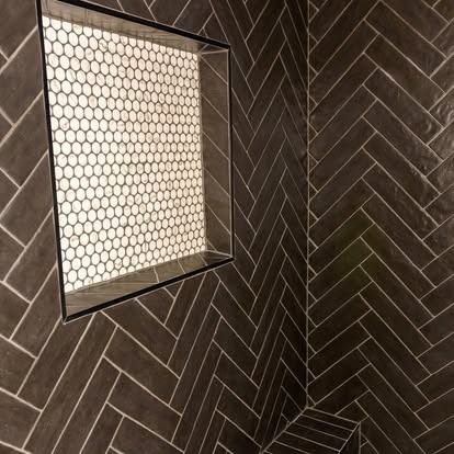Dark herringbone tile shower wall with a small hexagonal-tile window
