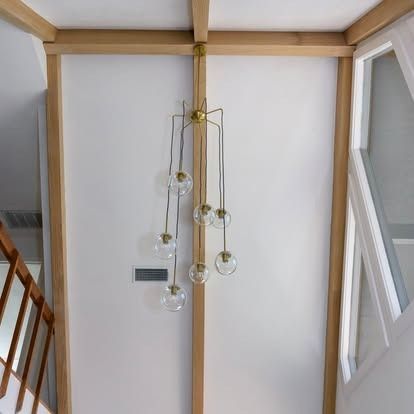 Modern pendant chandelier with glass globes hanging in a bright stairwell above wooden railings