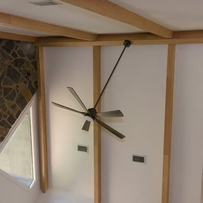 Modern wall clock with long black hands on a beige wall with wood trim and a stone accent