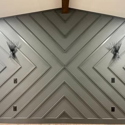 Interior wall with gray chevron paneling, decorative branches, and small wall lights
