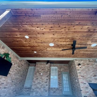 Covered brick porch with wood-paneled ceiling, ceiling fan, recessed lights, and white door.
