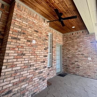 Brick front porch with wood ceiling, black ceiling fan, and glass-paneled door under an overhang