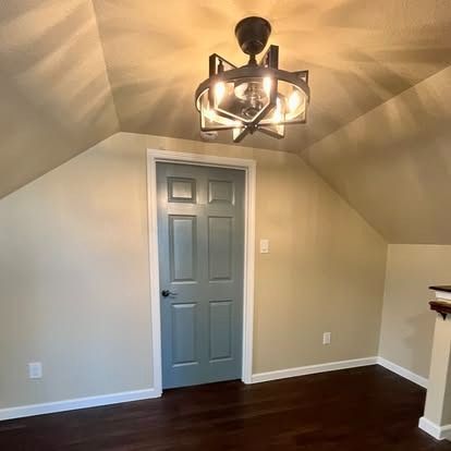 Empty room with beige walls, dark wood floor, gray door, and modern ceiling light fixture.