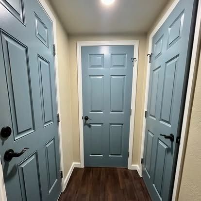 Narrow hallway with four light blue paneled doors and dark wood flooring