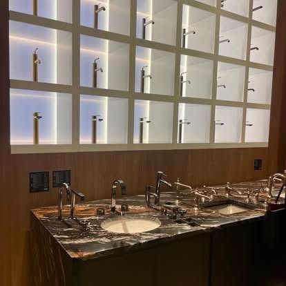 Modern restroom vanity with marble sinks, chrome faucets, and illuminated display shelving above.