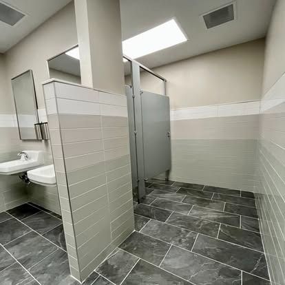 Modern public restroom with stalls, sinks, gray tile floor, and frosted glass partitions