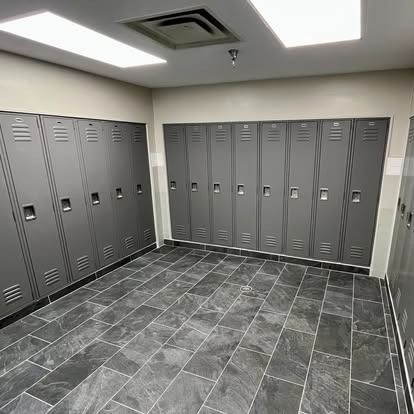 Empty locker room with gray lockers, tiled floor, and ceiling lights