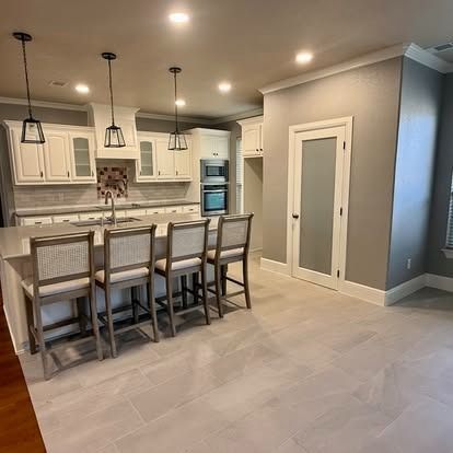 Modern kitchen with white cabinets, gray island seating, and pendant lights over light tile flooring