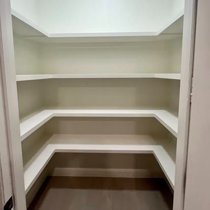 Empty walk-in closet with white built-in shelves and hanging space above a brown floor.