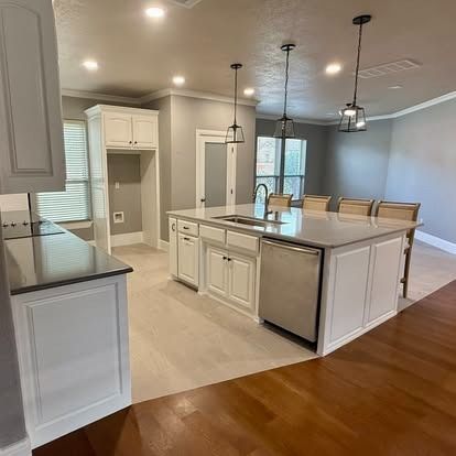 Bright modern kitchen with white cabinets, large island, pendant lights, and hardwood floors leading to a dining area