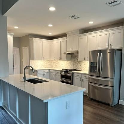 Bright modern white kitchen with stainless steel appliances, island, and dark wood floors