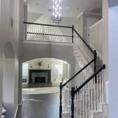 Bright foyer with curved staircase, black-and-white railings, and fireplace visible through an arched opening.