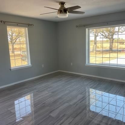 Empty gray living room with large windows, glossy floors, and a ceiling fan