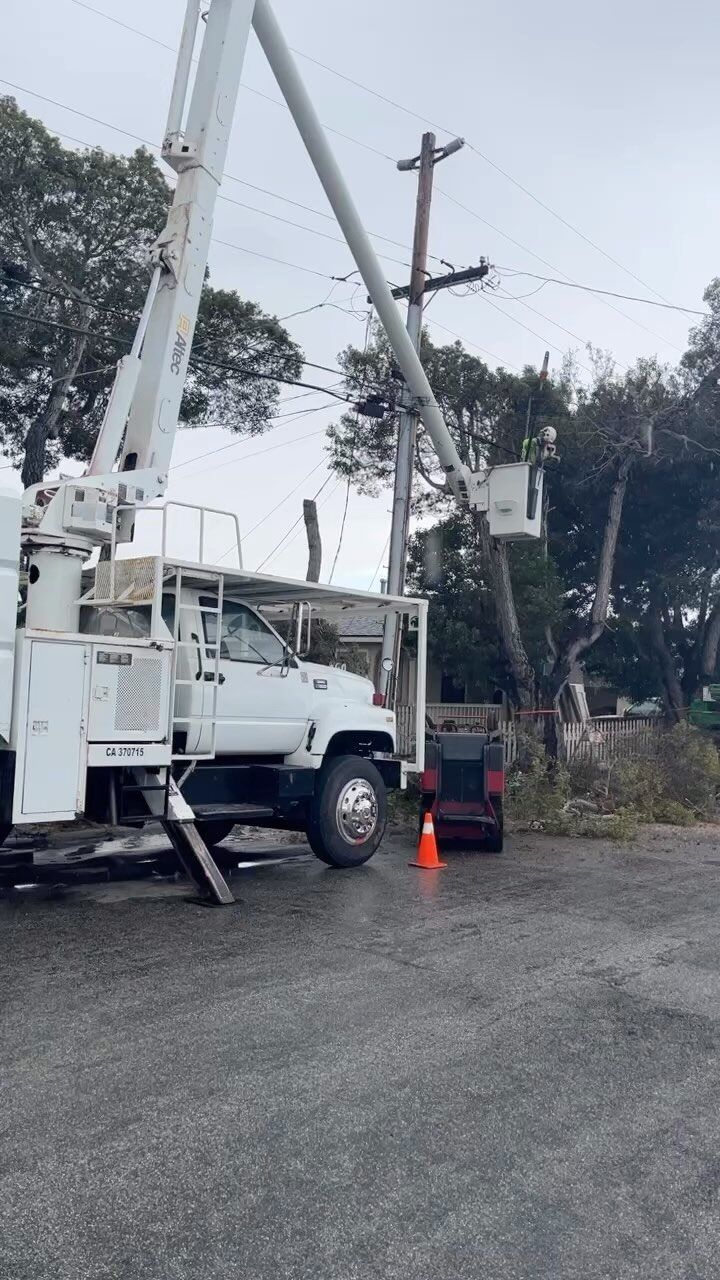 A utility truck with a raised boom working on a telephone pole. Orange cone on wet pavement.