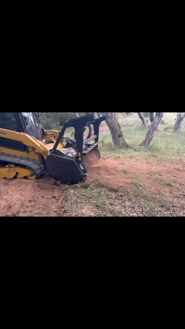 Skid steer clearing brush in a wooded area; dust and dirt fly into the air.