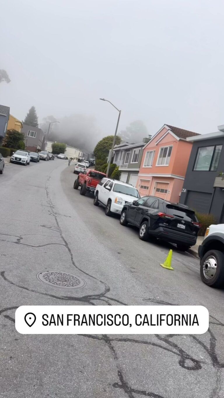 A San Francisco street with parked cars, foggy sky, and colorful houses.