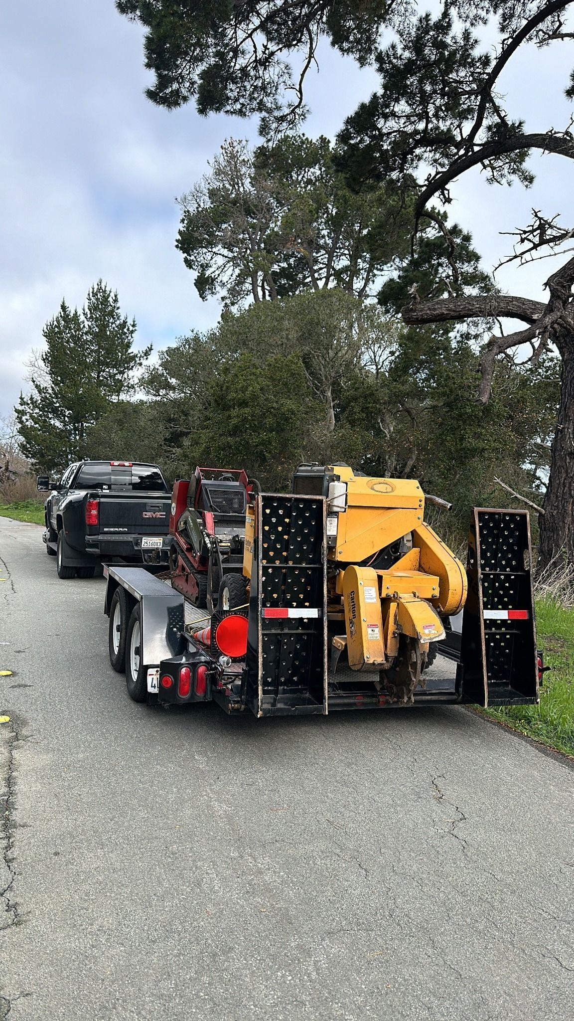 Truck pulling a trailer with a yellow wood chipper parked on a paved road.