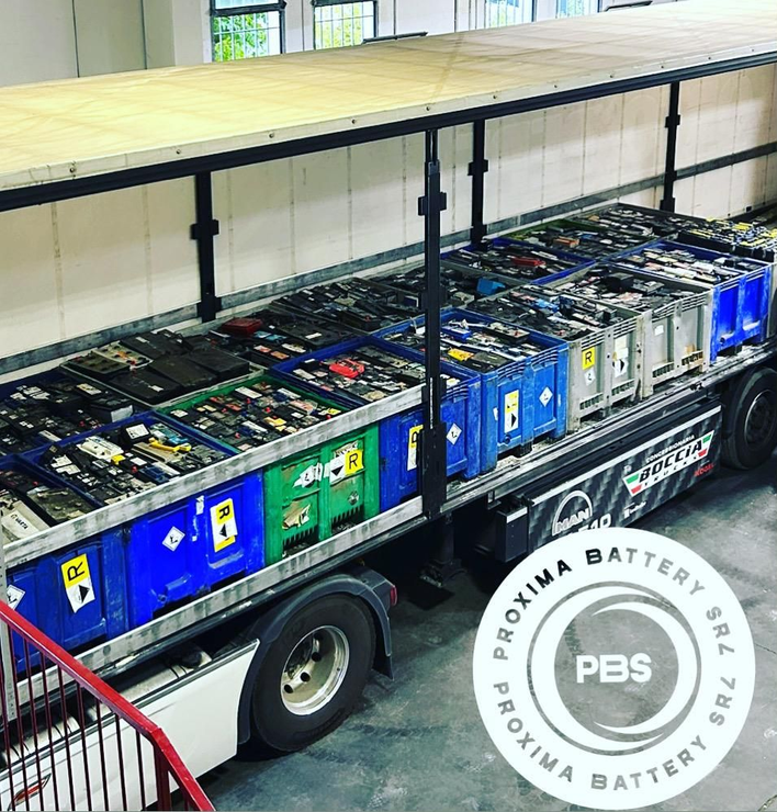 Un rimorchio carico di pile di contenitori per batterie industriali, con il logo di Proxima Battery sovrapposto in basso a destra.