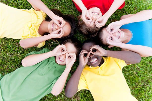 Children lying in a circle on grass, smiling and making heart shapes with their hands
