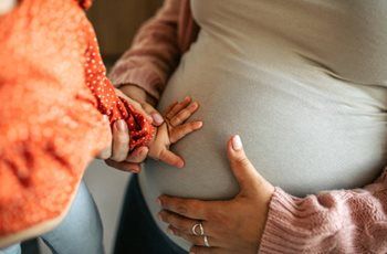Pregnant person holding hands with another person in a supportive moment.
