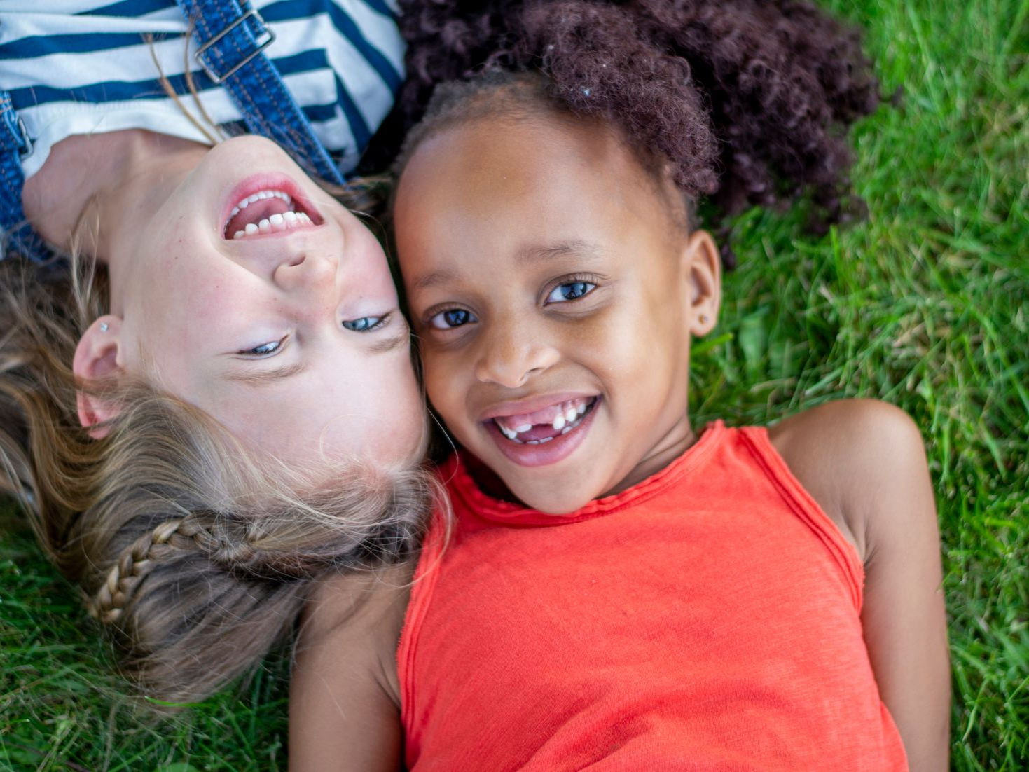 Two children lying on grass, smiling and looking up at the camera