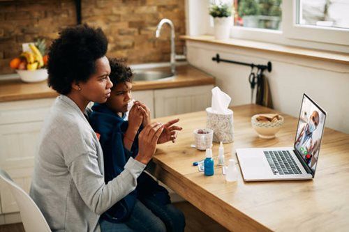 Two people sitting at a kitchen table on a video call with a laptop