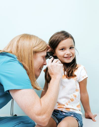 Woman taking a photo of a smiling child sitting against a light blue background